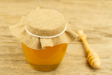 glass jar of honey closed jute cloth drizzler on wooden background