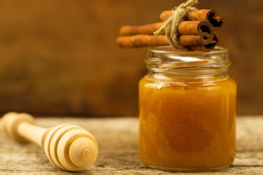 small jar of honey with drizzler and cinnamon on wooden background