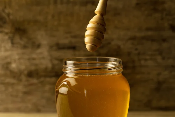 Tarro de vidrio de miel con rociador sobre fondo de madera — Foto de Stock