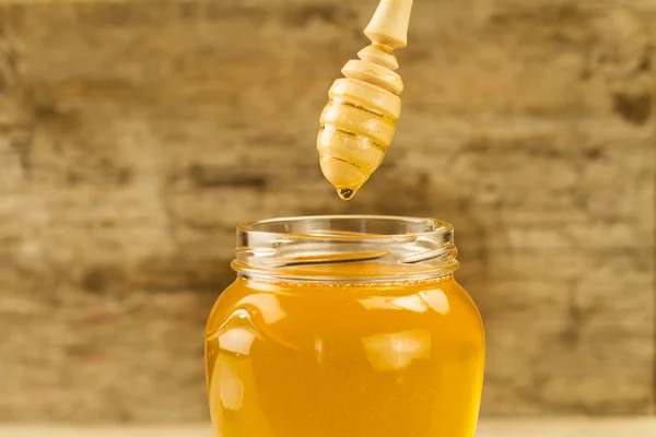 Glass jar of honey with drizzler on wooden background — Stock Photo, Image