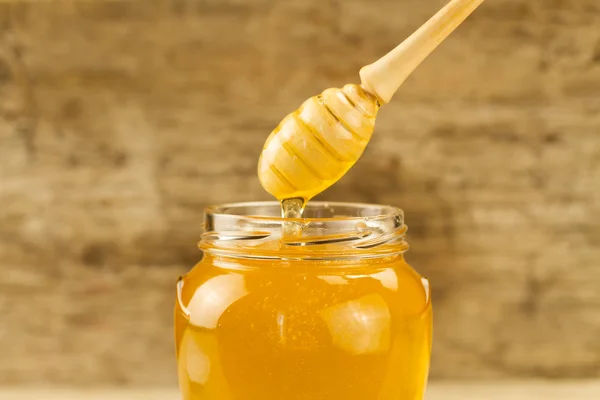 Tarro de vidrio de miel con rociador sobre fondo de madera —  Fotos de Stock