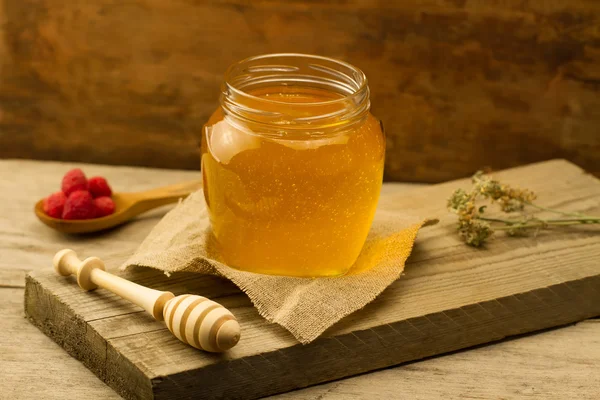 Cam Kavanoz bal ile drizzler, ahududu, jüt kumaş, ahşap arka plan üzerinde kuru çiçekler