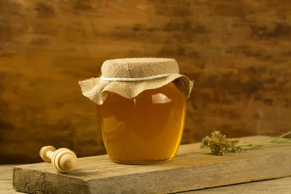 Glass jar of honey with drizzler, jute fabric, dried flowers on wooden background — Stock Fotó