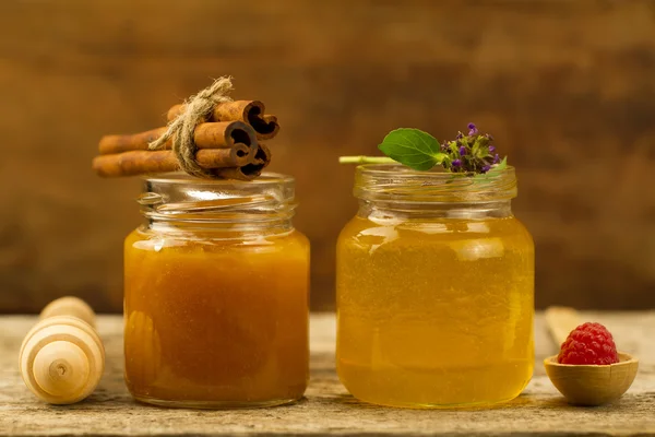 two small jars of fresh honey with cinnamon, flowers, raspberries on wooden background