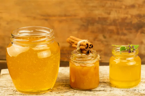 Three jars of honey with cinnamon, flowers on wooden background — Stok fotoğraf