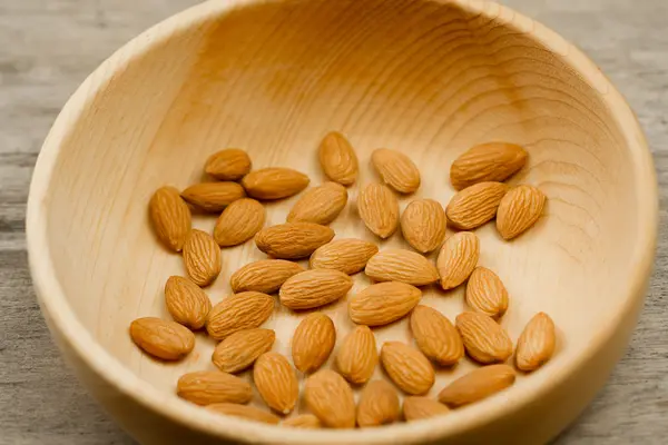 Kupas almond di piring pada latar belakang kayu. Untuk vegetarian. — Stok Foto