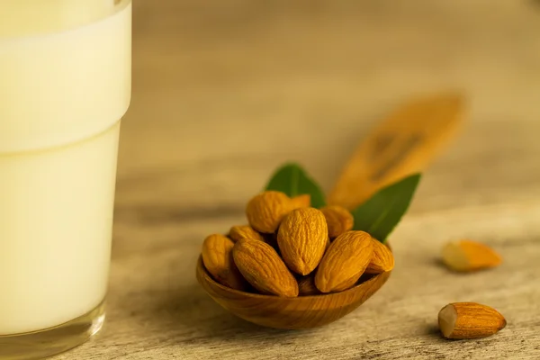 Peeled almonds in a spoon c leaves and a glass of milk on wooden table — Stock Photo, Image