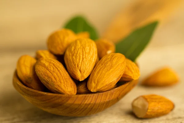 Peeled almonds in a spoon c leaves on wooden table — Stock Photo, Image