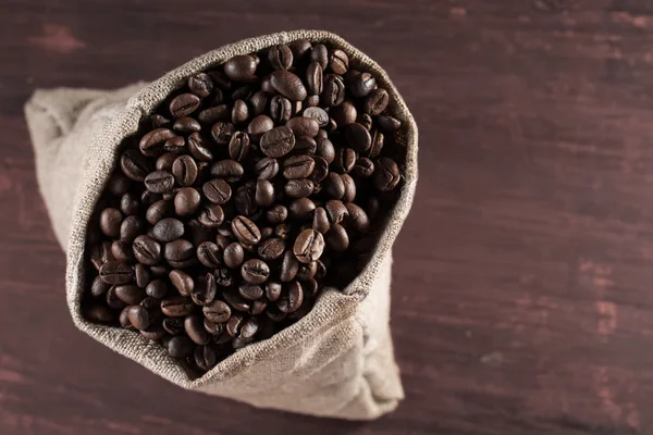 Kaffebönor i säckväv säck på trä bakgrund — Stockfoto