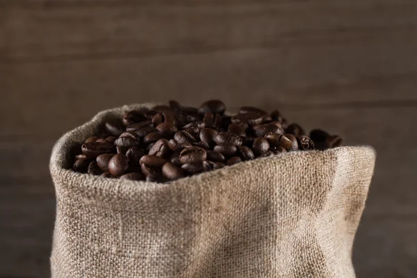 Granos de café en saco de arpillera sobre fondo de madera — Foto de Stock