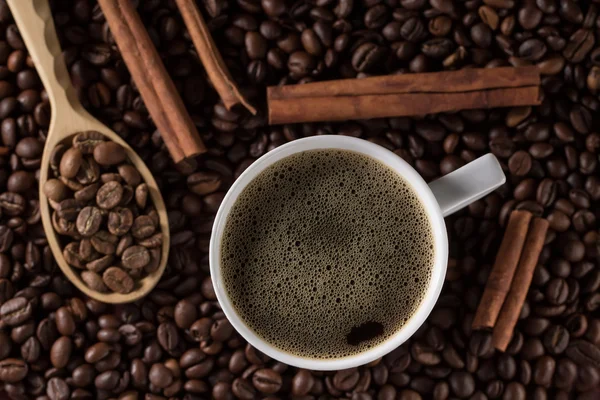 Cup of brewed French coffee with cinnamon sticks and wooden spoon on a background beans