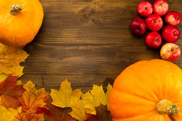 Yellow ripe pumpkin, maple leaves, red apples on wooden background. Thanksgiving, autumn. Stock Picture