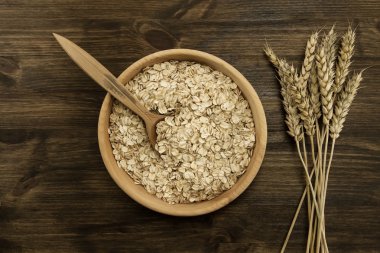 oatmeal flakes in a wooden bowl with a spoon, ears of wheat on the table. homemade, menu, recipe, mock up