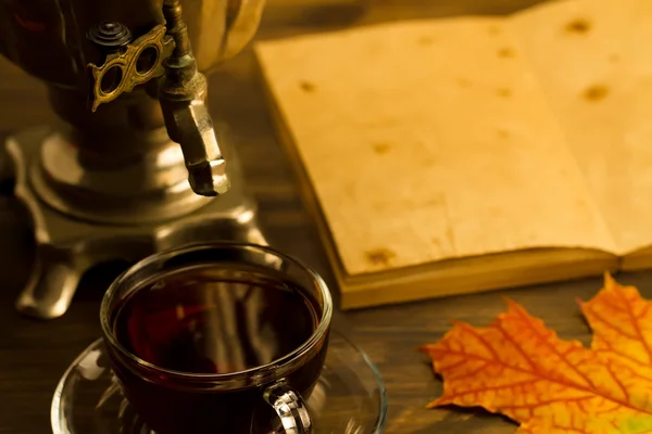Tea still life with samovar, maple leaves, on wooden background. Empty open an old vintage book. Russia autumn.