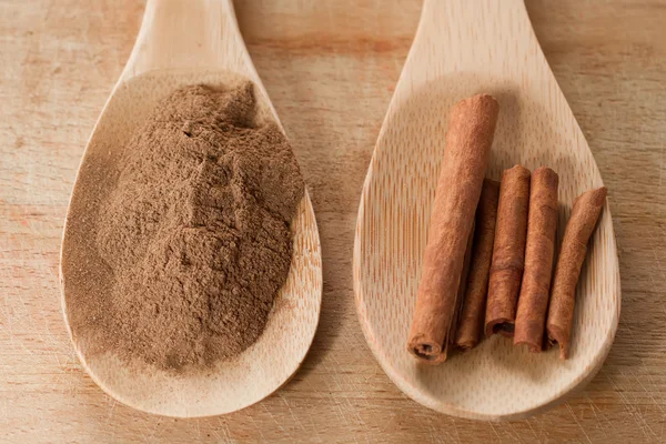 Whole cinnamon sticks and powder in spoon on wooden background — Stock Photo, Image