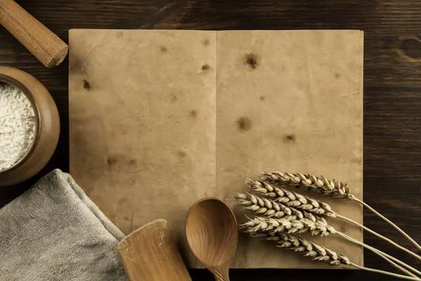 open old vintage book on the aged wooden background. Kitchen utensils, ears of wheat, flour in a pot. homemade, menu, recipe, mock up