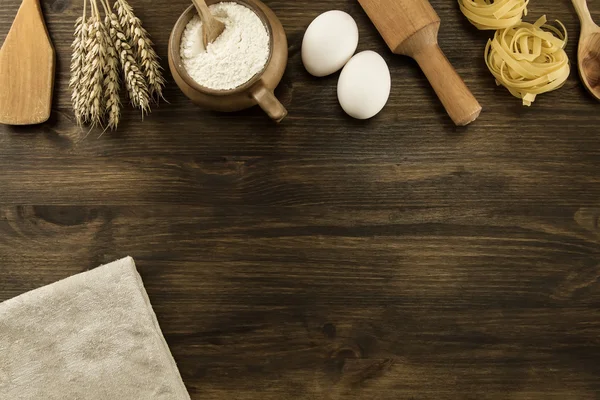 Pot of flour, wheat ears, pasta, eggs, kitchen utensils on wooden background. homemade, menu, recipe, mock up — Stock Photo, Image