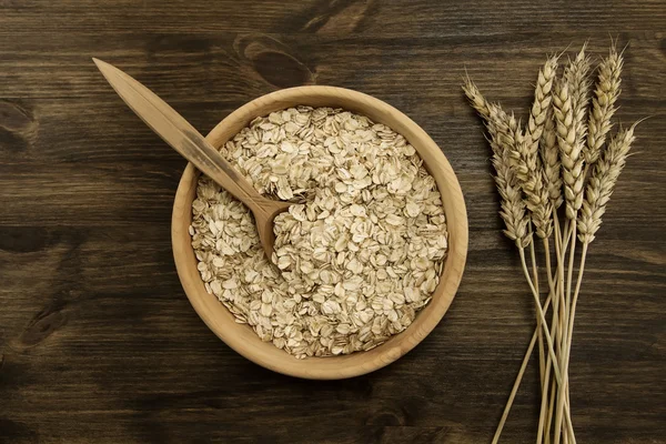 oatmeal flakes in a wooden bowl with a spoon, ears of wheat on the table. homemade, menu, recipe, mock up
