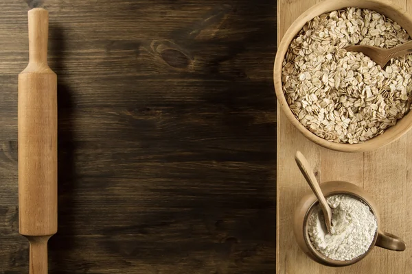 oatmeal flakes in a wooden bowl with a spoon, ears of wheat, pot of flour, kitchen utensils on the table. homemade, menu, recipe, mock up.