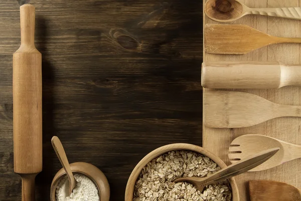 Copos de avena en un tazón de madera con una cuchara, espigas de trigo, olla de harina, utensilios de cocina en la mesa. casero, menú, receta, maqueta . — Foto de Stock