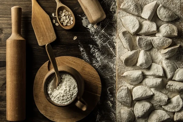 Ravioles de pasta casera sobre mesa de madera con harina. utensilios de cocina — Foto de Stock