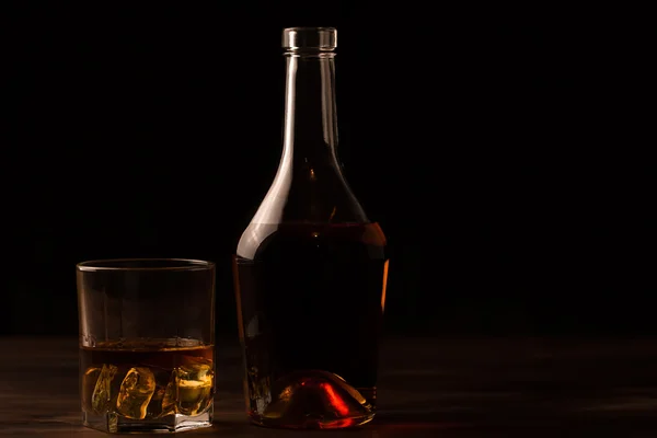 Vaso de whisky con hielo y una botella sobre una mesa de madera. Coñac, brandy . — Foto de Stock