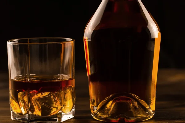 Vaso de whisky con hielo y una botella sobre una mesa de madera. Coñac, brandy . — Foto de Stock