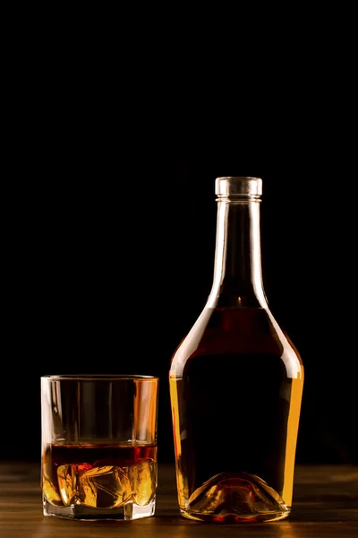 Copo de uísque com gelo e uma garrafa em uma mesa de madeira. Conhaque, conhaque . — Fotografia de Stock