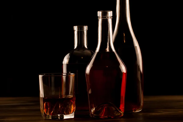 Glass of whiskey with ice and a bottle on a wooden table. Cognac, brandy. — Stock Photo, Image