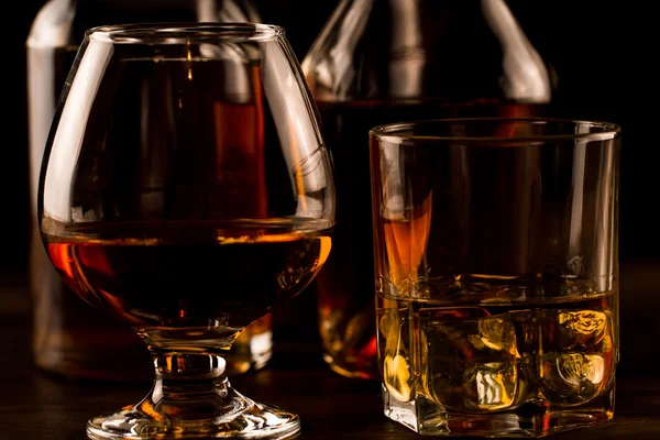 Vaso de whisky con hielo y una botella sobre una mesa de madera. Coñac, brandy . — Foto de Stock