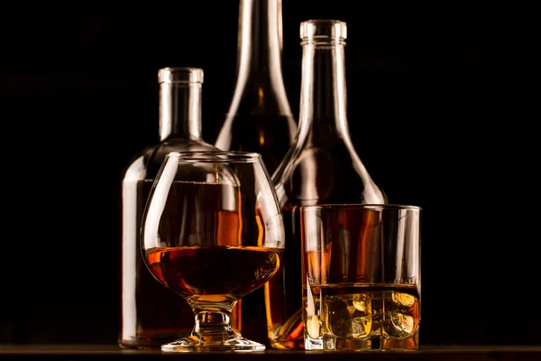 Склянка віскі з льодом і пляшка на дерев'яному столі. Коньяк, бренді . — стокове фото