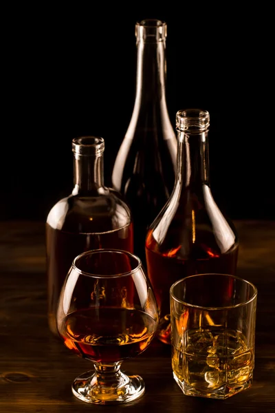 Glass of whiskey with ice and a bottle on a wooden table. Cognac, brandy. — Stock Photo, Image