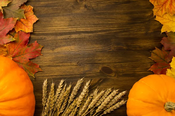 Gelber reifer Kürbis, Ahornblätter, rote Äpfel, Weizen auf hölzernem Hintergrund. Erntedank, Herbst, hausgemacht. Stockfoto