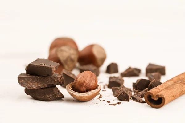 Broken chocolate bar, hazelnut and cinnamon on wooden background, close-up — Stock Photo, Image