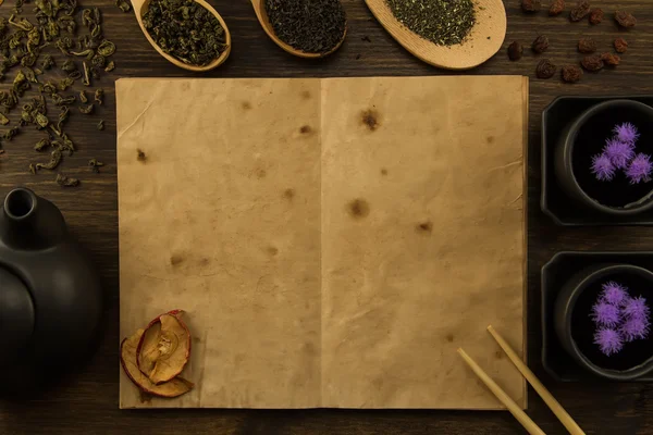 Zwarte theepot twee kopjes thee collectie, bloemen, oude open notitieboek op houten achtergrond. Menu, recipe, mock up — Stockfoto