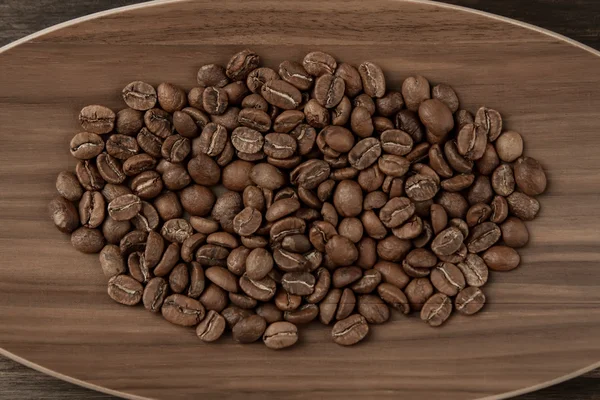 Жареные кофейные зерна на тарелке на деревянном фоне. Вид сверху — стоковое фото