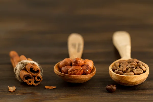 Shelled hazelnuts, roasted coffee beans, cinnamon on wooden background, close up — Stock Photo, Image