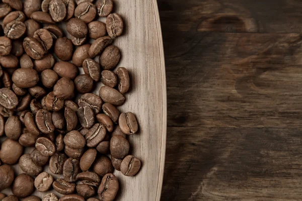 Granos de café asados en el plato sobre fondo de madera. Vista superior — Foto de Stock