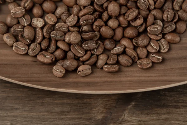Granos de café asados en el plato sobre fondo de madera. Vista superior — Foto de Stock