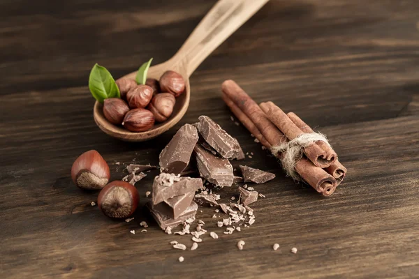 Broken chocolate bar, hazelnut and cinnamon on wooden background, close-up — Φωτογραφία Αρχείου