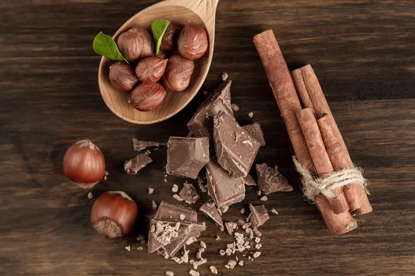 Broken chocolate bar, hazelnut and cinnamon on wooden background, close-up — Stock fotografie