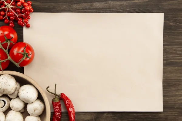Blatt altes Vintage-Papier mit Tomaten, Champignons, Chilischoten auf gealtertem Holzgrund. gesunde vegetarische Kost. Rezept, Menü, Attrappe, Kochen. Stockbild