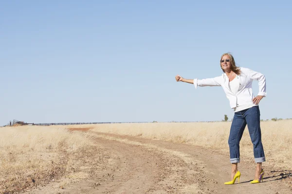 Hitchhiking woman in high heels at dirt road — Stock Photo, Image