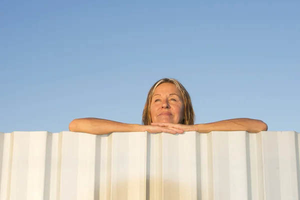 Happy friendly woman leaning relaxed over fence — Stock Photo, Image