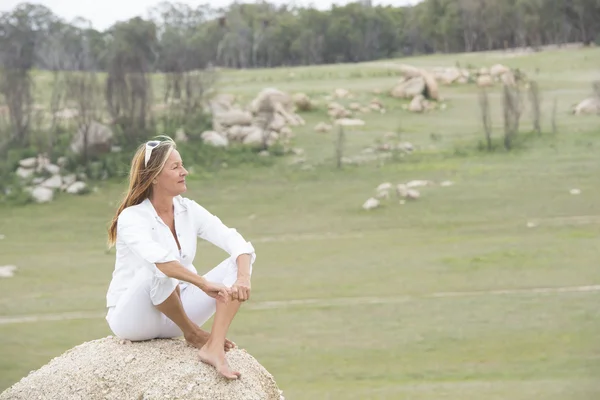 Happy relaxed woman outdoor sitting on rock — Stock Photo, Image