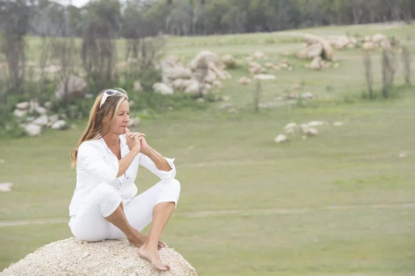 Thoughtful woman outdoor sitting on rock — Stock Photo, Image