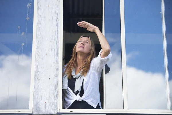 Bekymret kvinne som ser bekymret ut fra vinduet – stockfoto