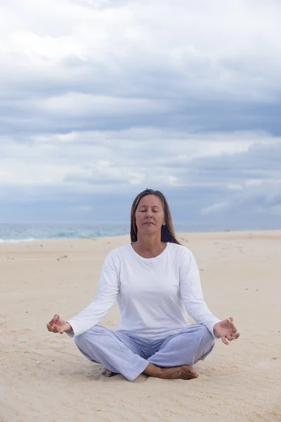 Mulher sênior meditando na praia — Fotografia de Stock