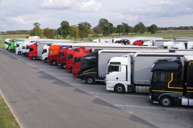 Dinlenme yeri. Otobanın dışındaki kalabalık bir otoparkta çeşitli kamyonlar var..