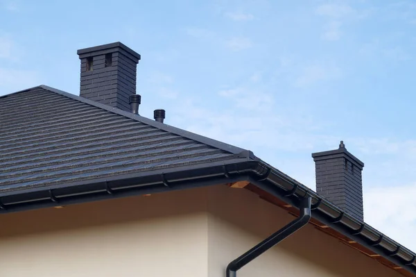 A newly built residential house. A fragment of the roof made of metal roof tiles, new chimneys.